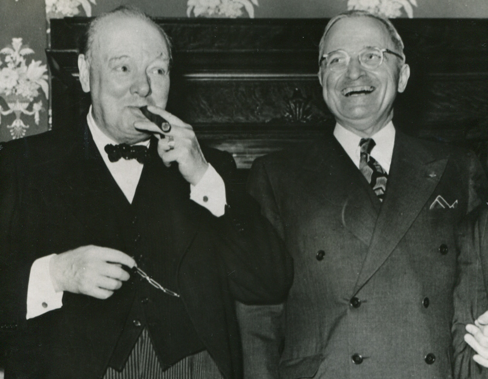 Churchill smoking a cigar, standing next to a laughing Truman